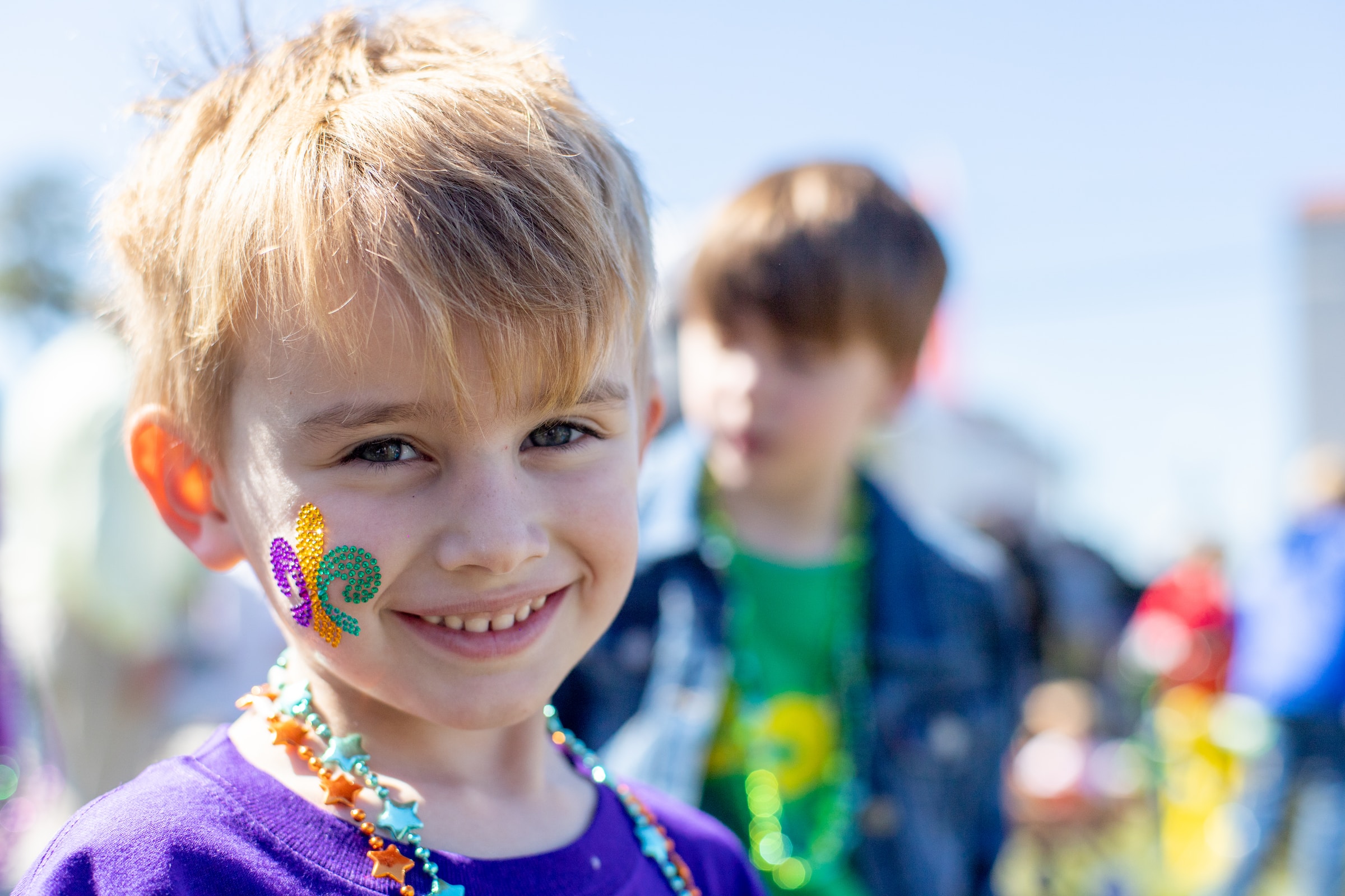 Smiling child with a Mardi Gras sticker on his face celebrating at a event