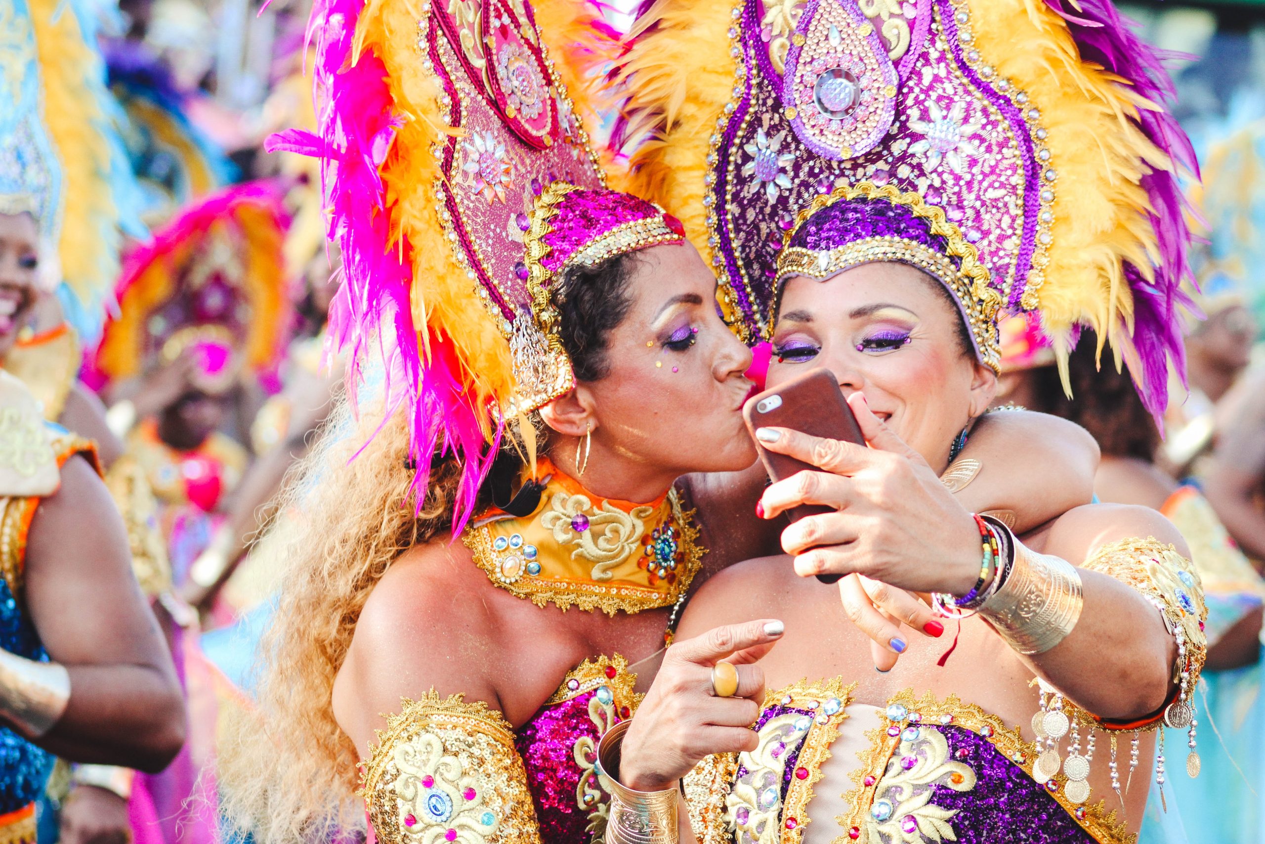 Two women in colorful Carnival costumes taking a selfie as one kisses the other on the cheek