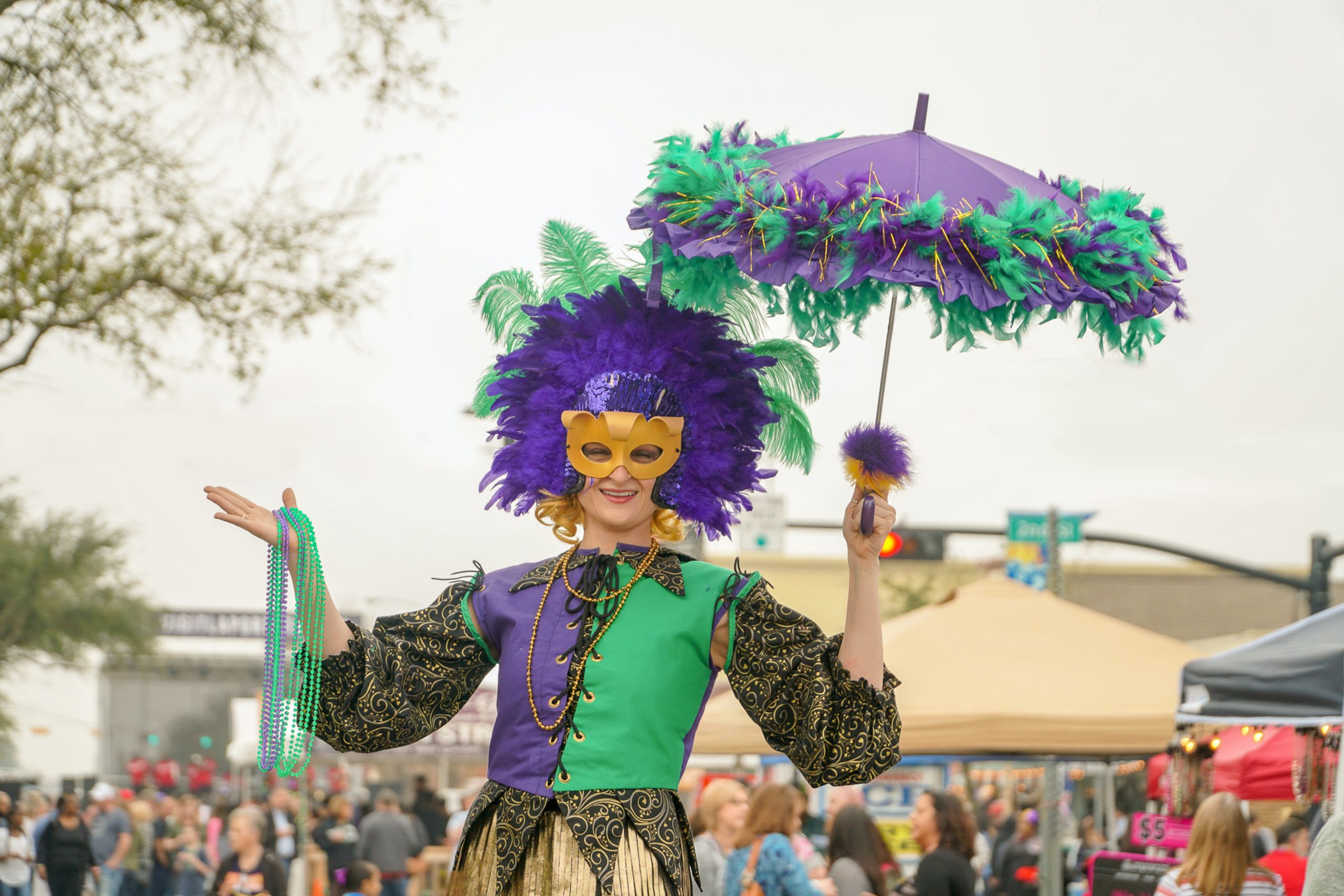 Person dressed festively in Mardi Gras colors holding a purple and green umbrella during celebration