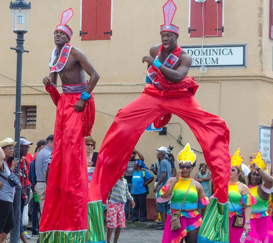 Two male Moko Jumbies on stilts performing in front of the Dominica Museum during Carnival