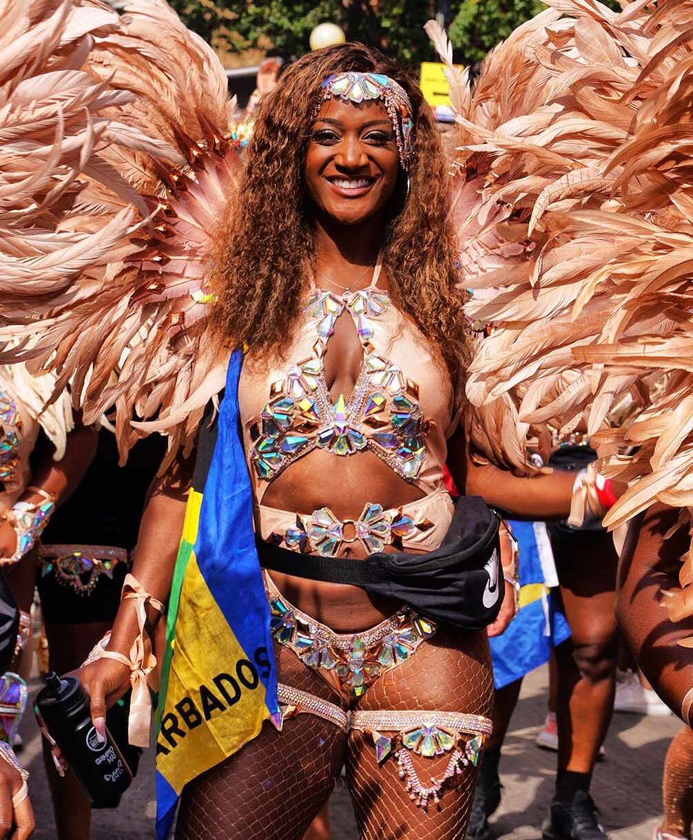 Masquerader wearing an elaborate gold costume and headdress holding the Barbados (Bajan) flag while performing in the Leicester Caribbean Carnival, UK.