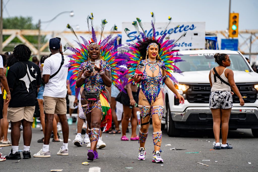 Two women in colorful Carnival costumes happily walking on the road at Toronto Caribbean Carnival.