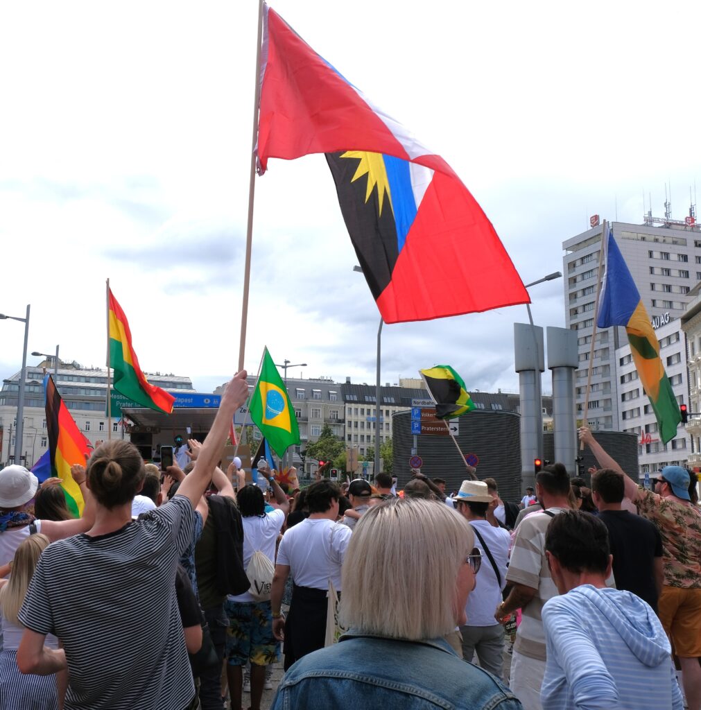Crowd of people celebrating with Caribbean flags in the sky at the Vienna Carnival Road March 2024, showcasing music, dance, and vibrant Caribbean culture in Austria.