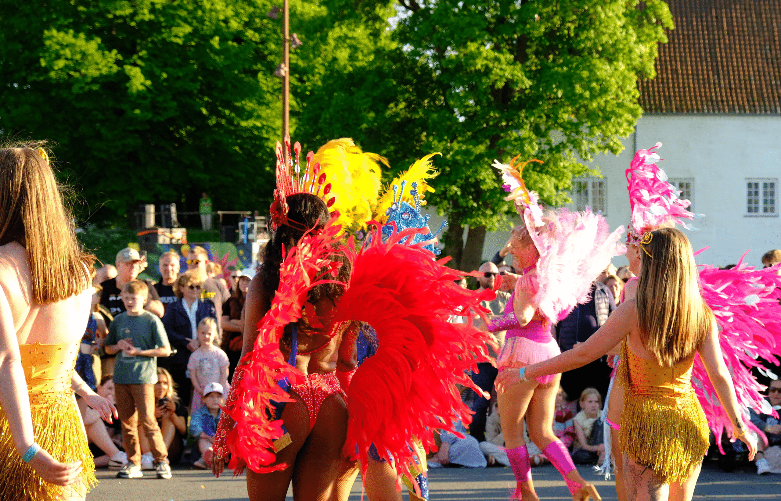 Female samba dancers in colorful feathered costumes seen from behind at Aalborg Karneval 2024 parade in Denmark.