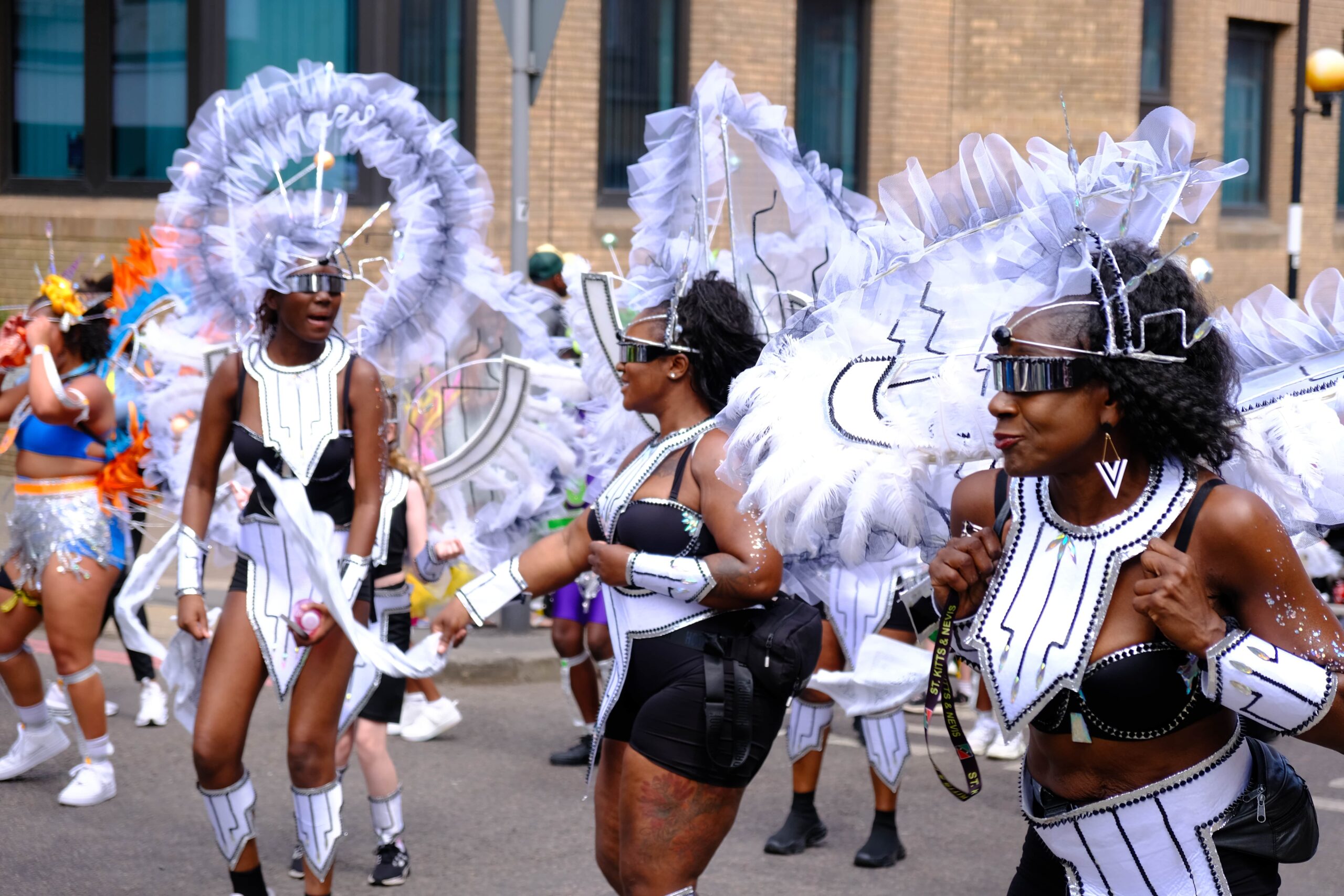 Masqueraders in vibrant Carnival costumes dancing and enjoying the road at Luton Carnival 2025 in the UK.