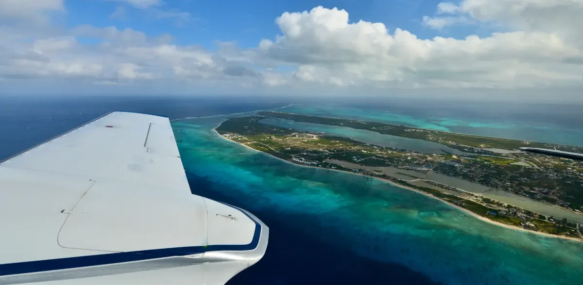 Airplane wing overlooking turquoise Caribbean waters and a tropical island coastline during arrival to a Caribbean destination.