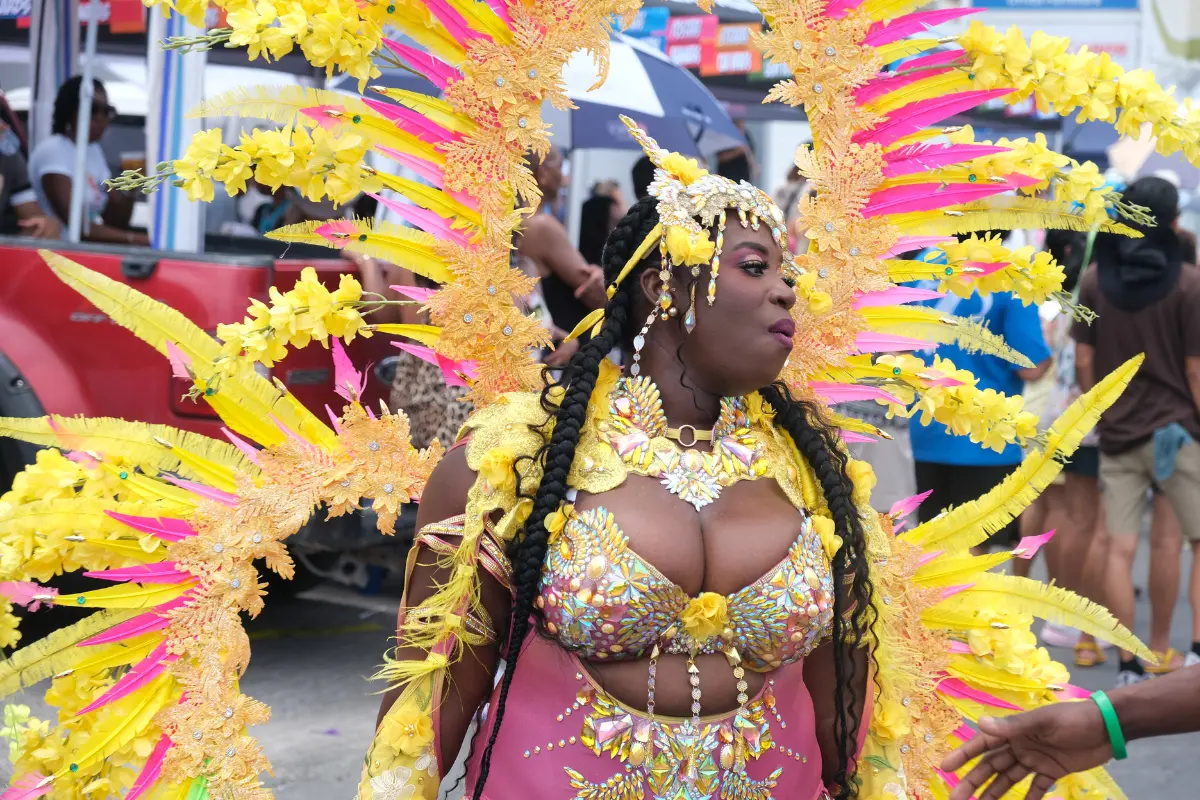 Close-up of a Sint Maarten Carnival masquerader wearing vibrant yellow feathers, intricate carnival makeup, and jeweled accessories during the parade.