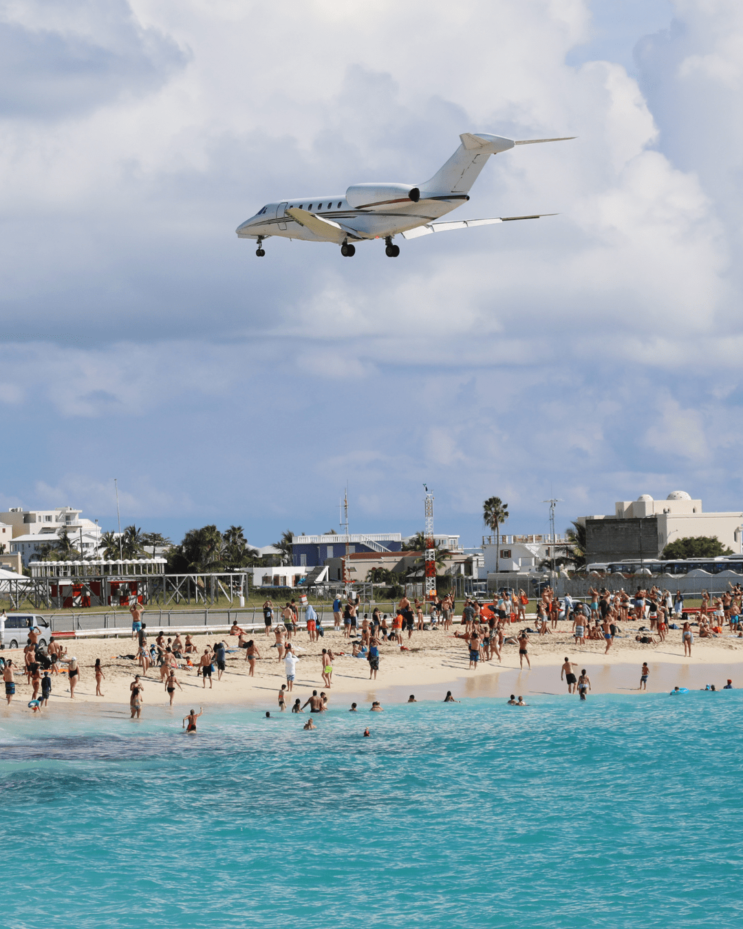 Small private plane flying low over Maho Beach in St. Maarten with beachgoers watching. A famous attraction near Carnival activities and SXM Carnival 2026 accommodations.