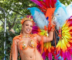 Woman in bright orange feathered costume and headpiece during Caribbean Carnival, representing mas band culture and key carnival terms.