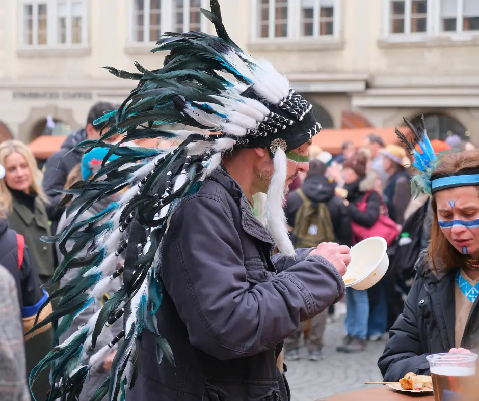 Masopust festival attendees in costume enjoying traditional Czech street food from bowls and plates during the lively celebration.