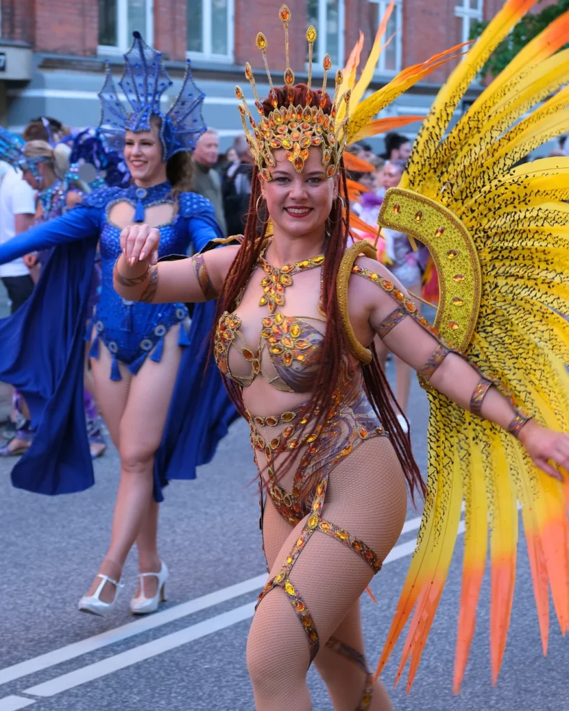 Female dancer in vibrant feathered costume performing during Aalborg Karneval parade in Aalborg, Denmark.