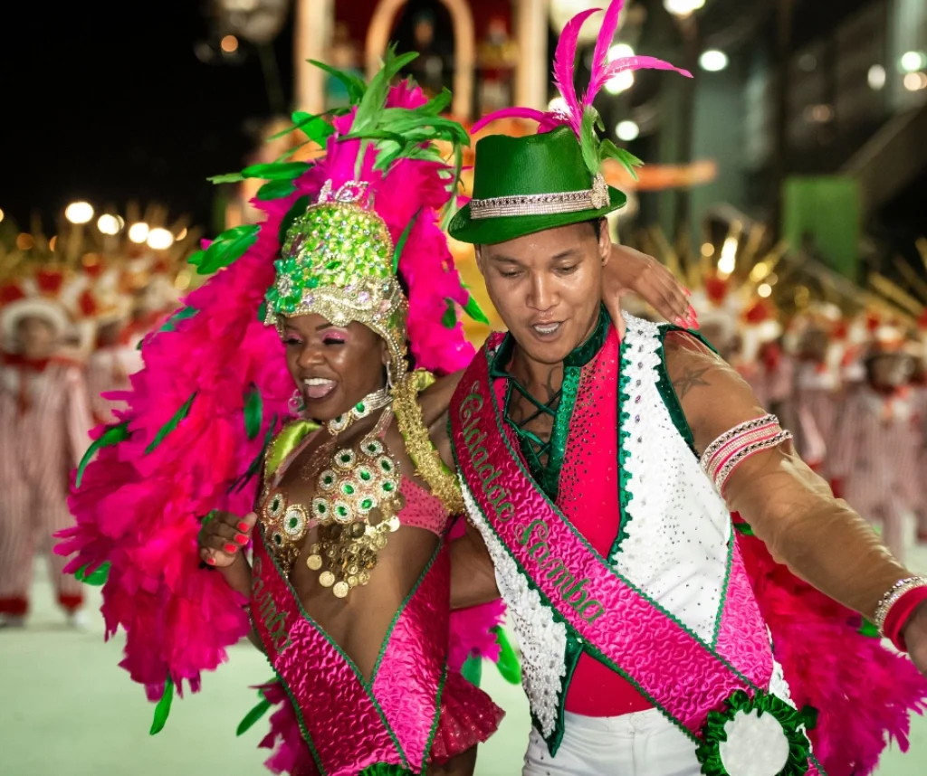 Two samba dancers in vibrant pink and green carnival costumes performing together during the Rio Carnival Sambadrome parade in Rio de Janeiro, Brazil.