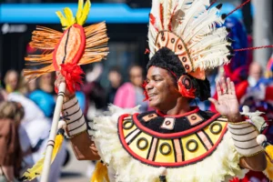Performer in ornate feathered costume at Verdenskarneval in Oslo, smiling and waving during the multicultural street parade.