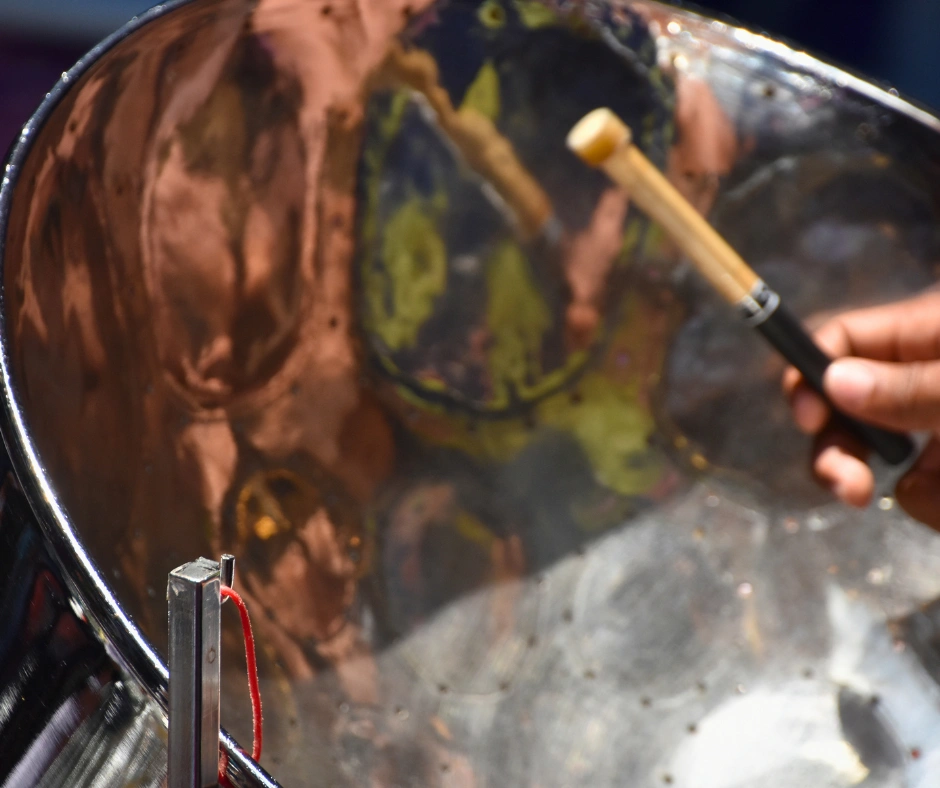 Close-up of a steelpan instrument being played with mallets, showing the tuned surface of the steel drum