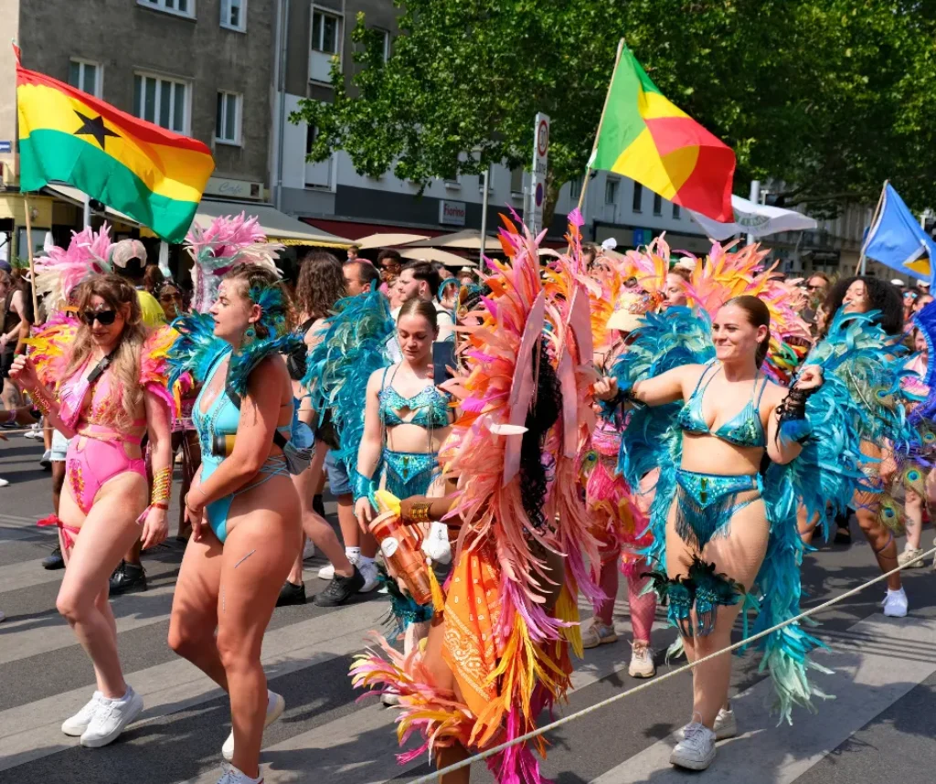 Colorful carnival parade with masqueraders in feathered costumes dancing in the street, showing what to expect when learning how to get a carnival costume and join a band