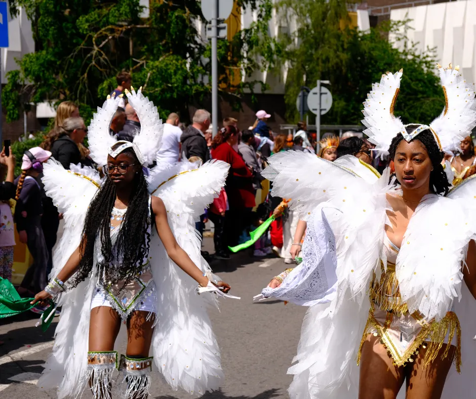 Masqueraders in white angel-themed carnival costumes with large feathered wings walking in a parade, representing themed sections when exploring how to get a carnival costume