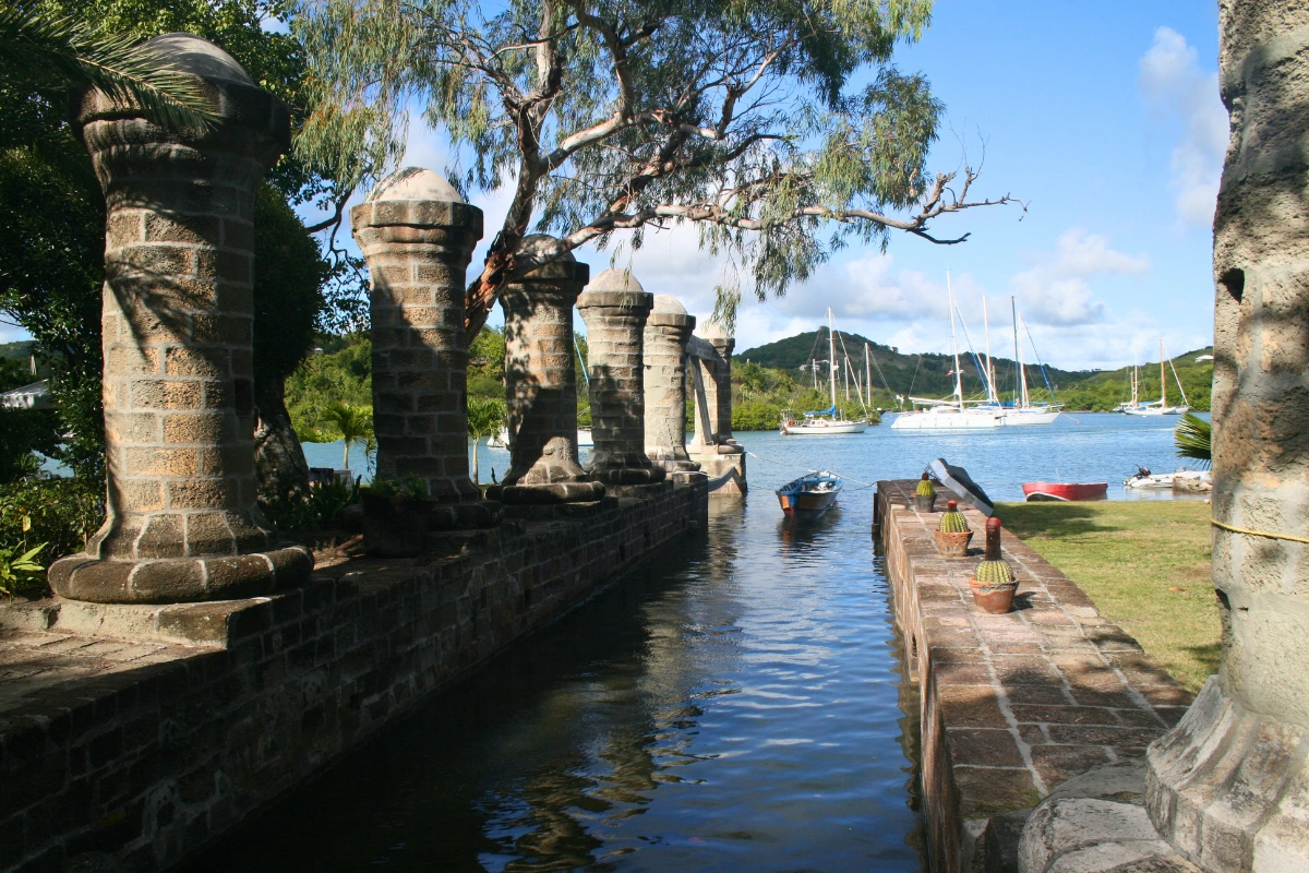 Historic stone pillars and waterfront at Nelson's Dockyard in English Harbour, Antigua, with sailboats anchored in the marina during a sightseeing tour.