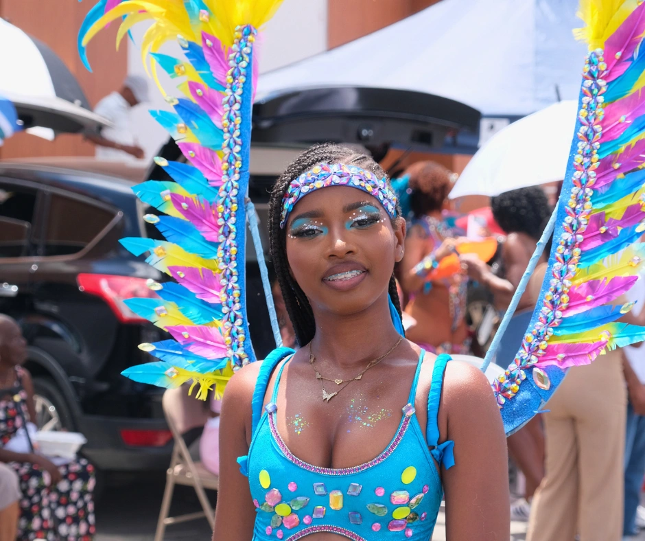 Carnival masquerader wearing a bright blue costume with yellow, pink, and turquoise feather wings, showing how to get a carnival costume for a vibrant parade look.