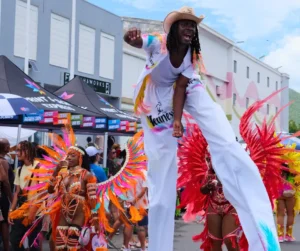 A stilt walker performs in white costume alongside colorful masqueraders during the SXM Carnival 2026 parade in St. Maarten.