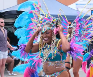 Smiling masquerader adjusting a colorful feathered carnival headpiece with turquoise, pink, and purple details, showing how to get a carnival costume for parade day.