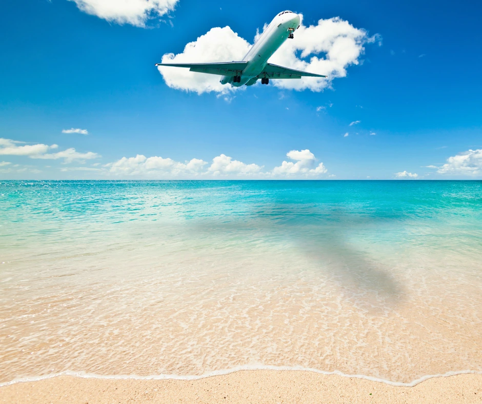 Airplane flying over turquoise Caribbean water in St Maarten during SXM Carnival season