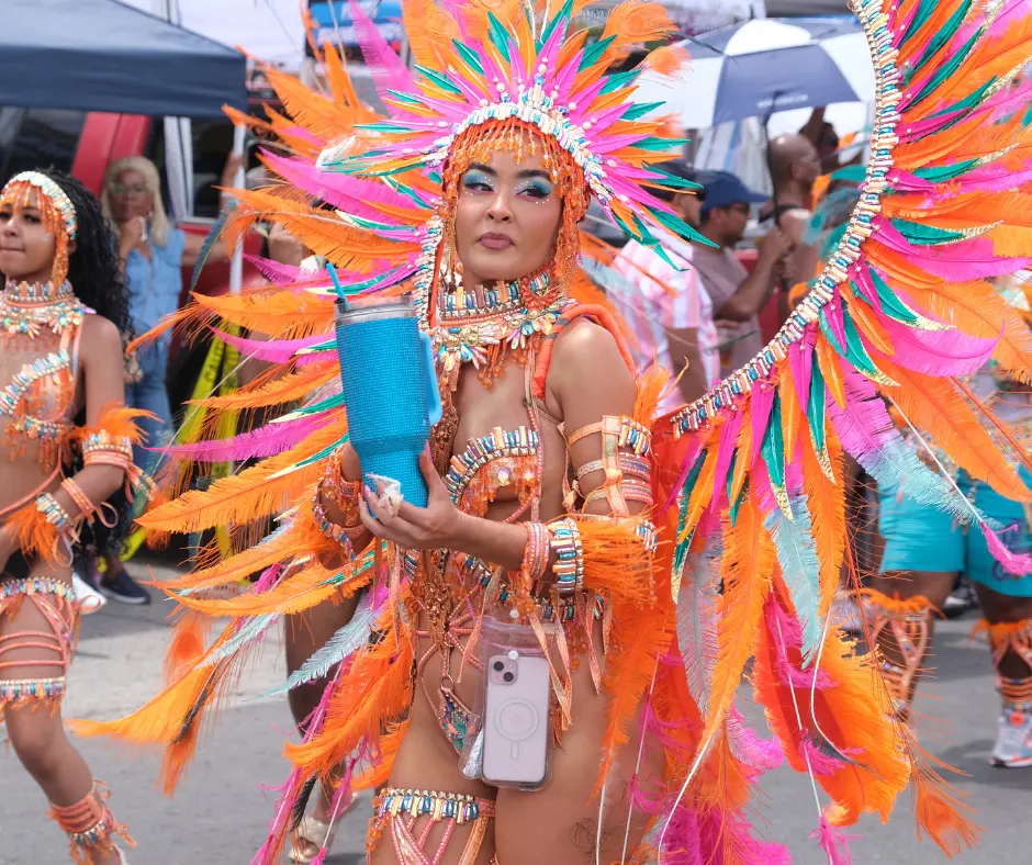 A masquerader wears a bright orange and pink feathered costume during the SXM Carnival 2026 grand parade.