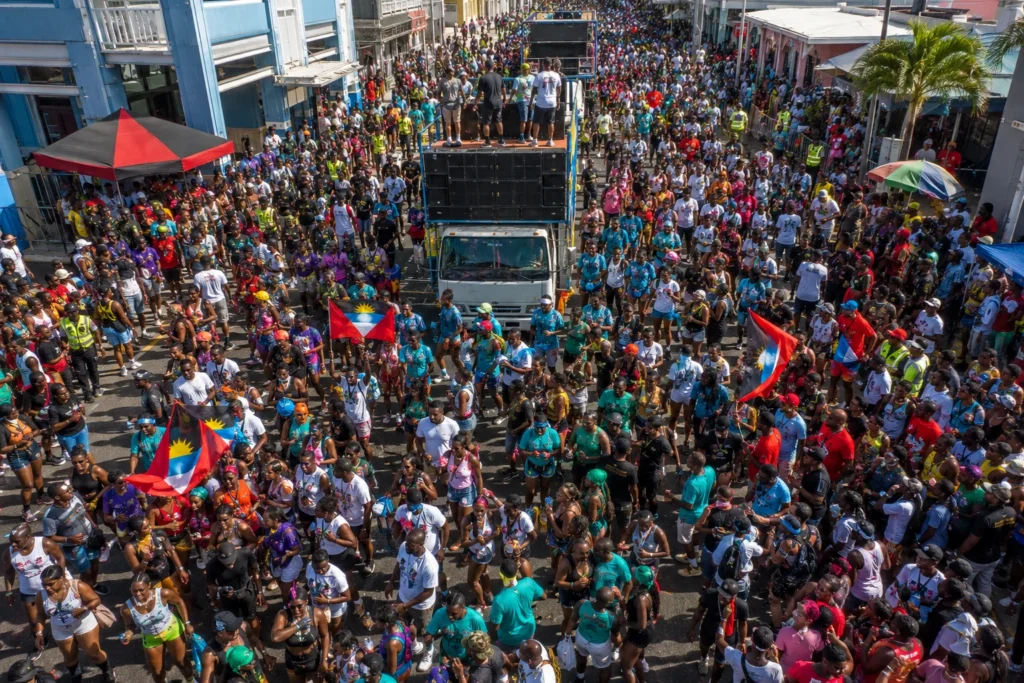 AI-generated aerial illustration of Antigua Carnival T-Shirt Mas in St. John’s showing revelers dancing behind music trucks during one of the top events on the list of Caribbean carnivals.