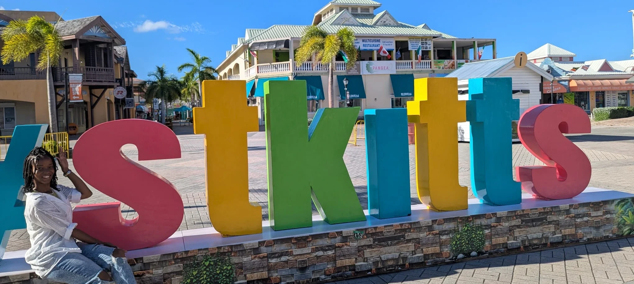 A visitor poses beside the colorful St. Kitts sign during a sunny Caribbean trip before SXM Carnival 2026.