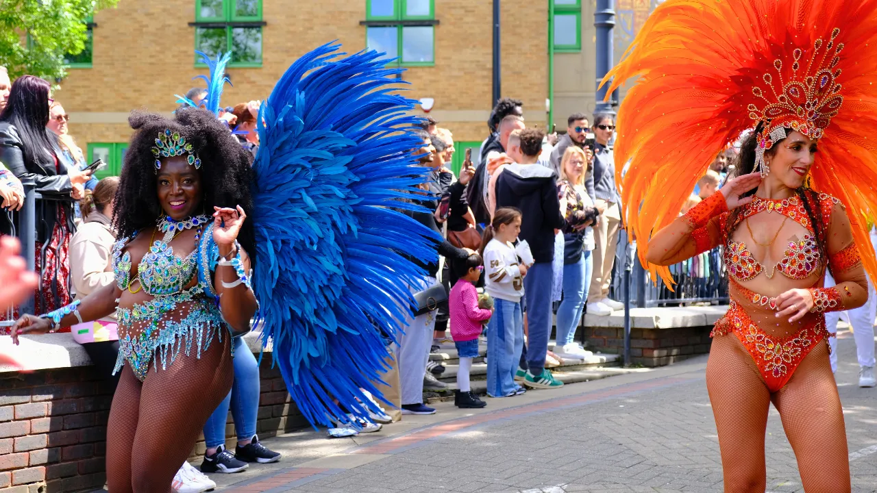 Two samba dancers in blue and orange feathered costumes performing together at Luton International Carnival