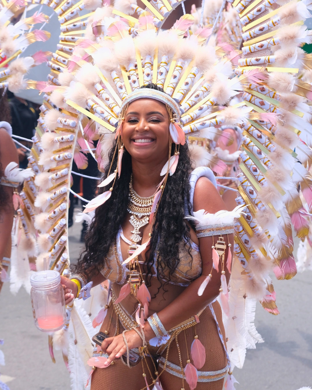 Smiling masquerader in soft pink and white feathered carnival costume, featured as a carnival travel resource