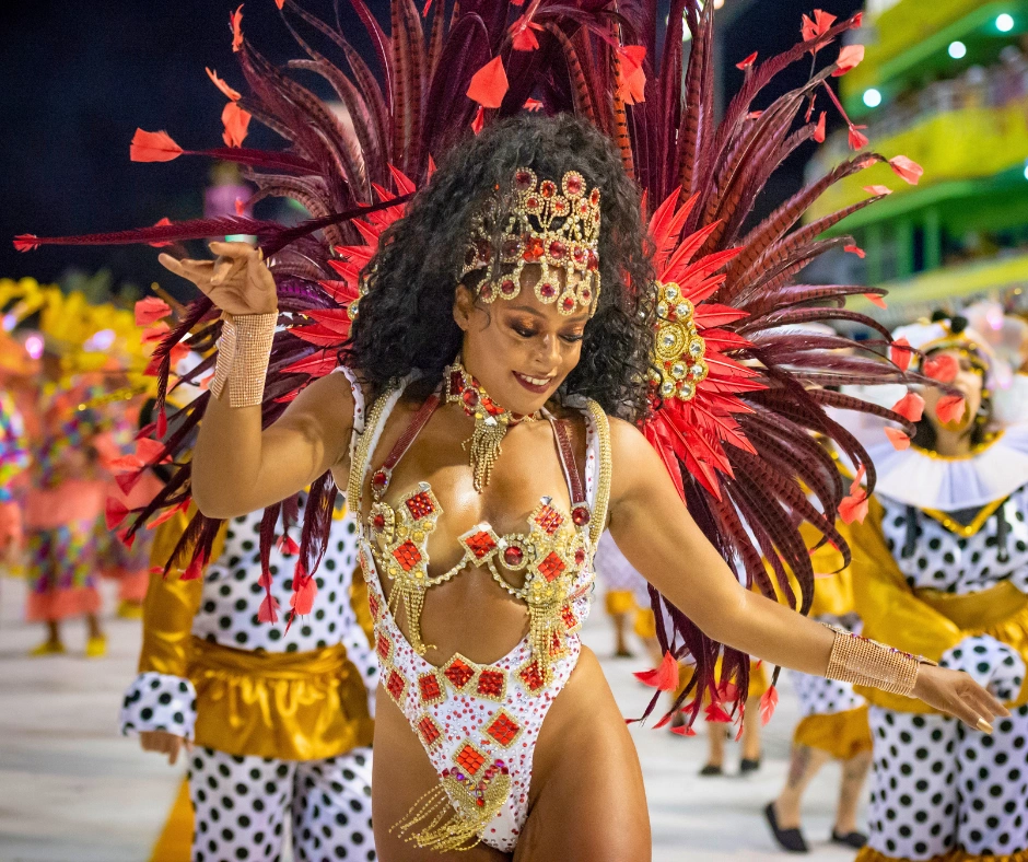 Samba dancer in a red and white jewelled costume with a large feathered headdress performing at the Rio Carnival Sambadrome at night