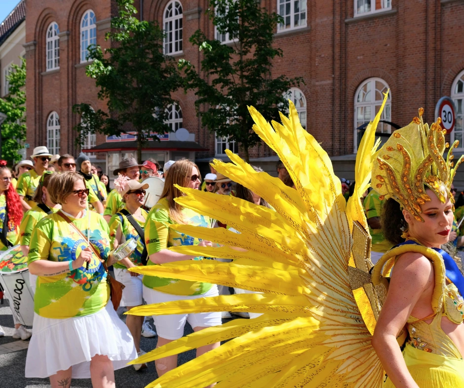 Performer in a dramatic yellow feathered backpack costume leading a samba band at the Berlin Carnival of Cultures