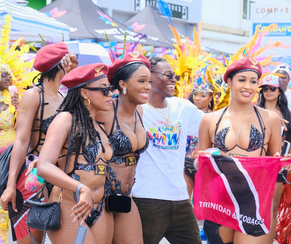 Masqueraders in black sequin costumes and red army berets playing mas at SXM Carnival with a Trinidad and Tobago flag on the road