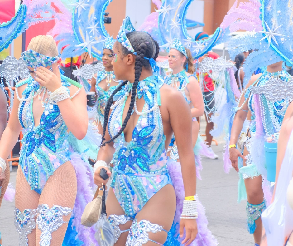 Women in matching blue and silver pretty mas costumes adorned with gems and feathers playing mas at SXM Carnival
