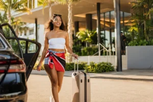 Traveller with a Trinidad and Tobago flag bandana arriving at a Miami hotel for Miami Carnival, rolling a suitcase past palm trees