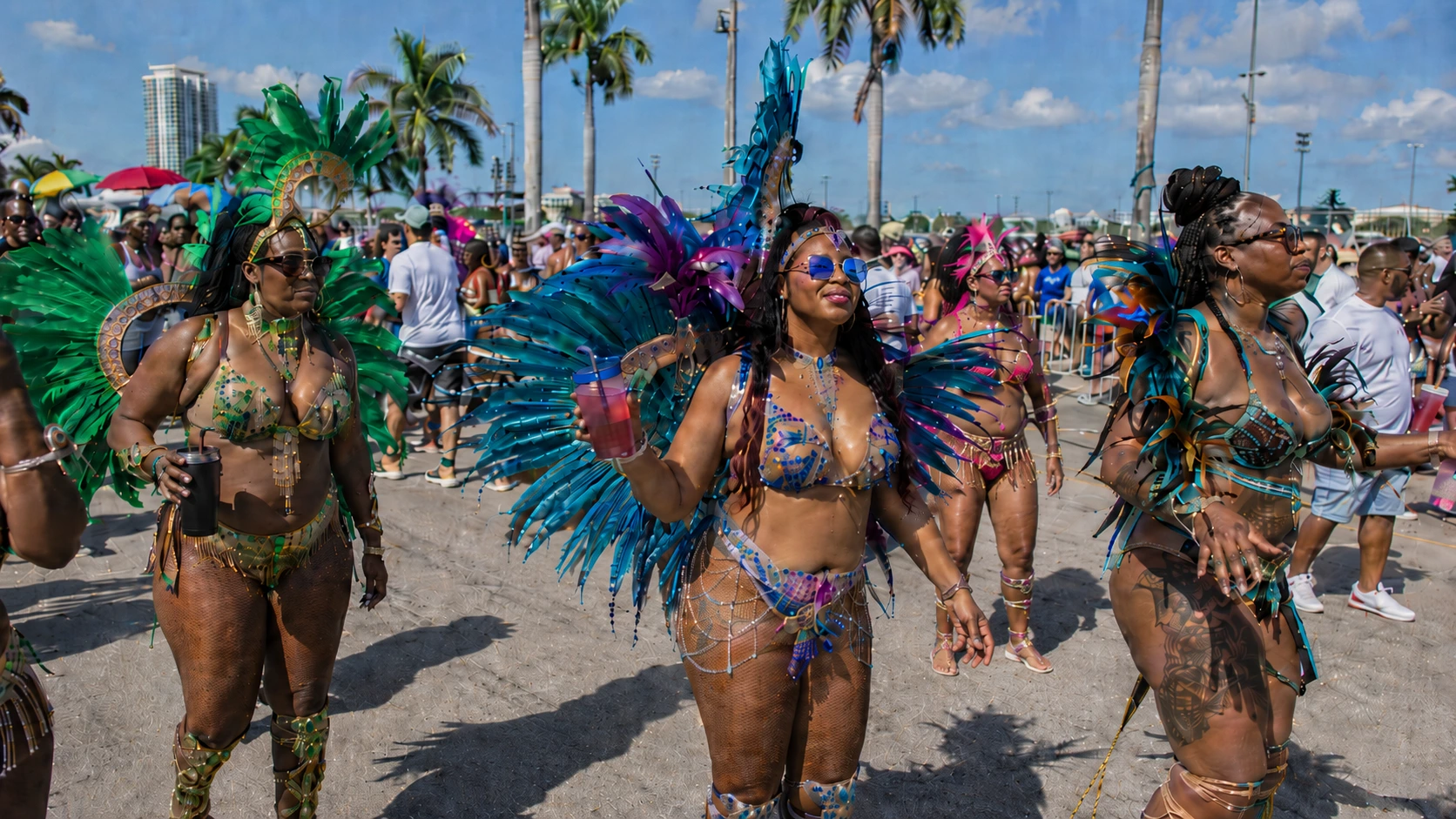 Miami Carnival masqueraders in purple, teal, and red feather costumes walking the parade route with the Miami skyline in the background