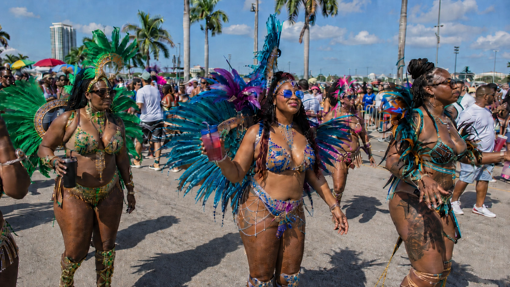 Miami Carnival masqueraders in purple, teal, and red feather costumes walking the parade route with the Miami skyline in the background