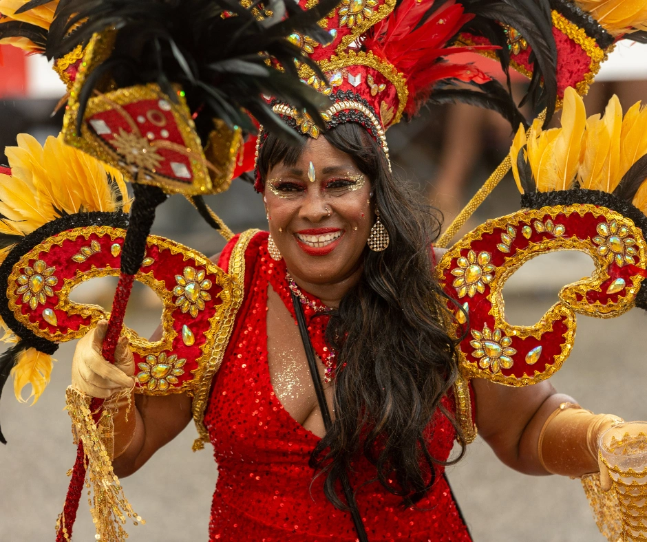 Masquerader in a red and gold feathered costume with a jewelled headdress and matching hand pieces