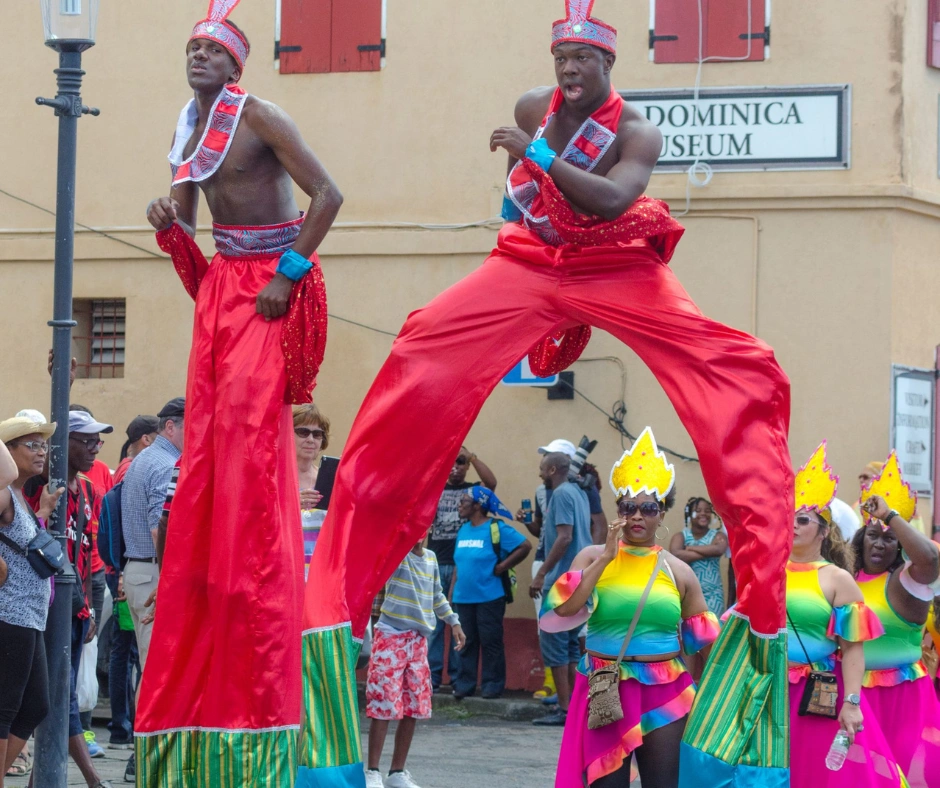 Two stilt walkers in red costumes towering over the crowd outside the Dominica Museum in Roseau during Carnival