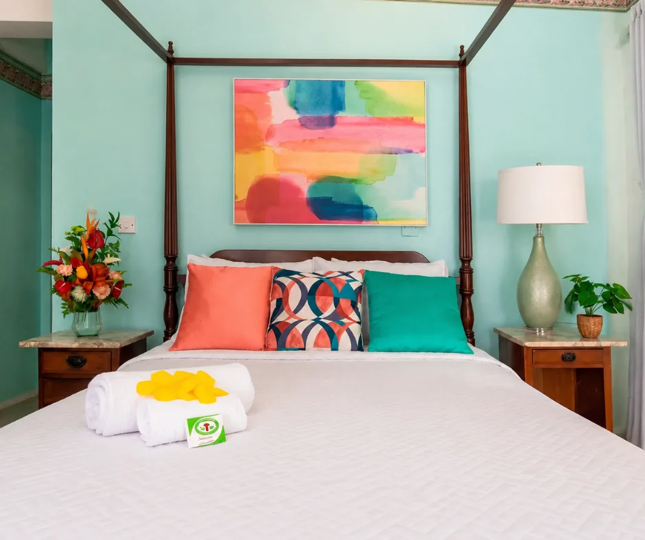 Four-poster bed and bright Caribbean artwork in a Sutton Place Hotel room, a central base for anyone deciding where to stay for Dominica Carnival.