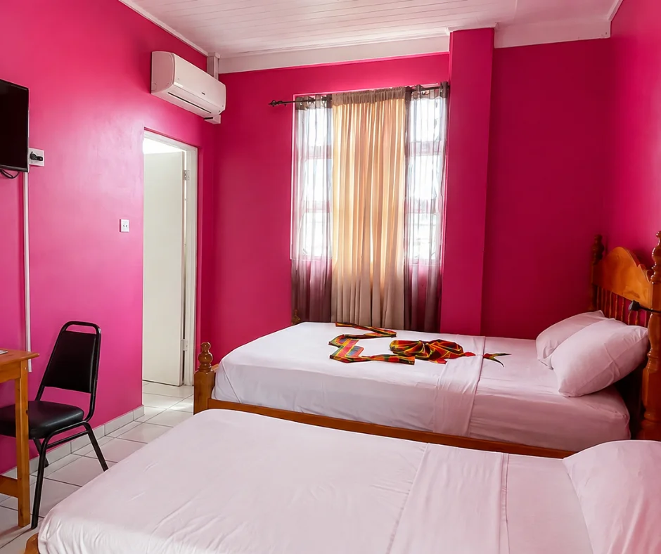 Twin beds and madras fabric detail in a pink guest room at La Flamboyant Hotel, a Dominica Carnival hotel on the King George V Street parade route.