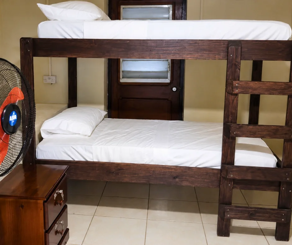 Wooden bunk beds and a floor fan in a dorm room at Roseau Hostel and Beach Front Property, the budget pick for where to stay for Dominica Carnival.