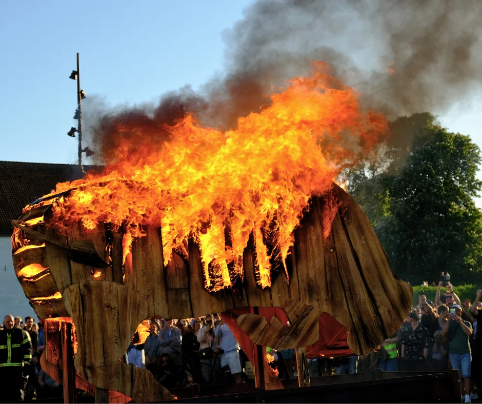 A large wooden bull effigy engulfed in flames as a crowd watches during Aalborg Karneval's Burning of the Bull