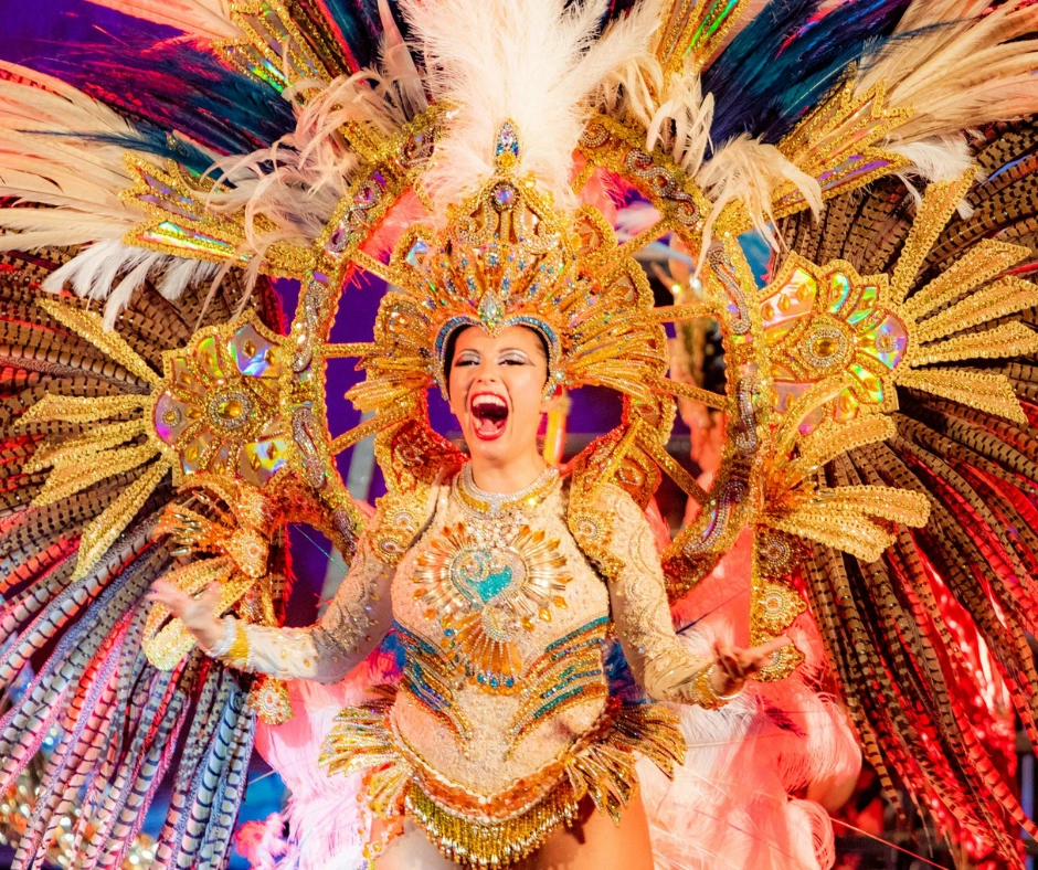 Comparsa dancer in a gold and cream feathered costume performing under stage lights at a night parade