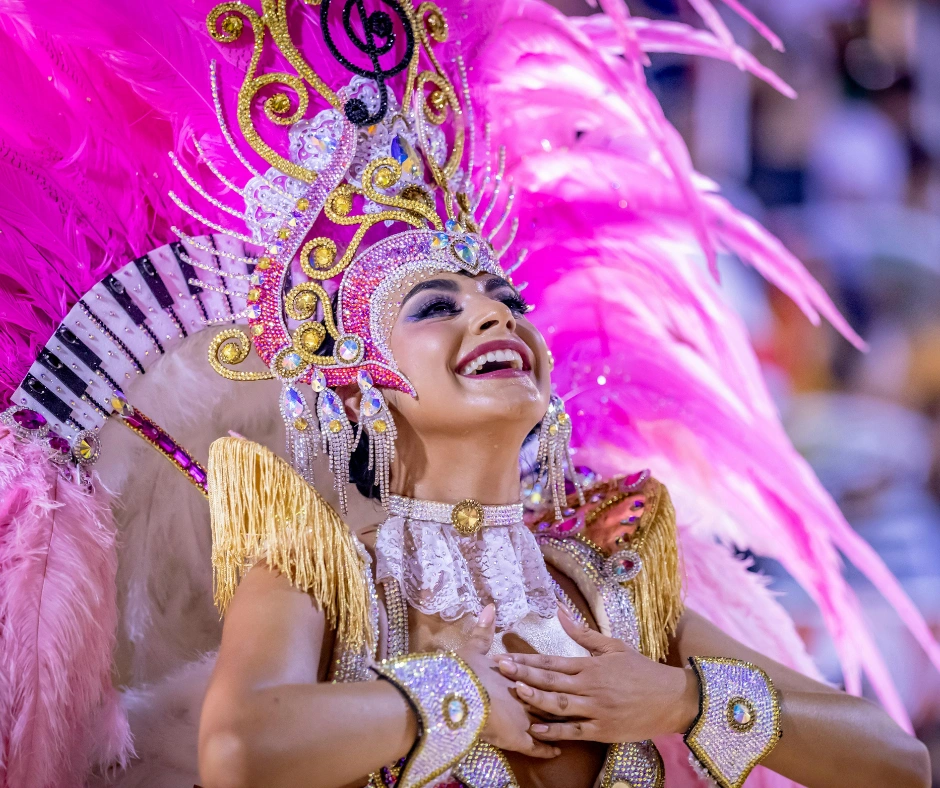 Comparsa dancer in a pink and silver feathered headdress smiling during a night sambadrome parade