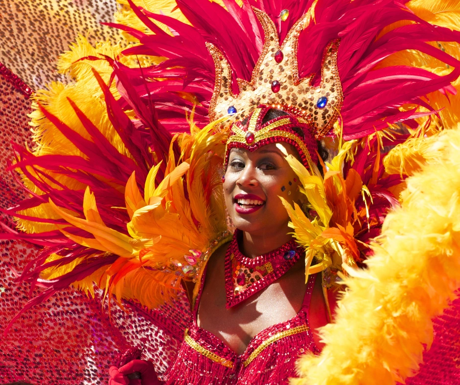 Masquerader in a red and orange feathered costume with a gold crown headpiece in bright sunshine