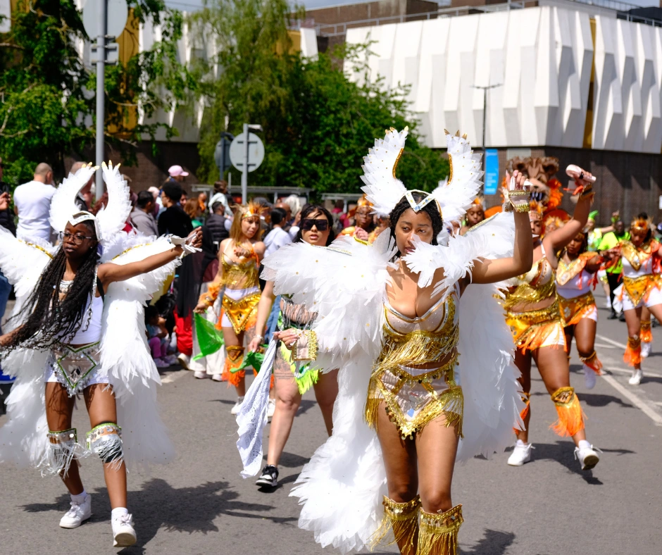 Masqueraders in white and gold feathered costumes dancing along a city street in daylight