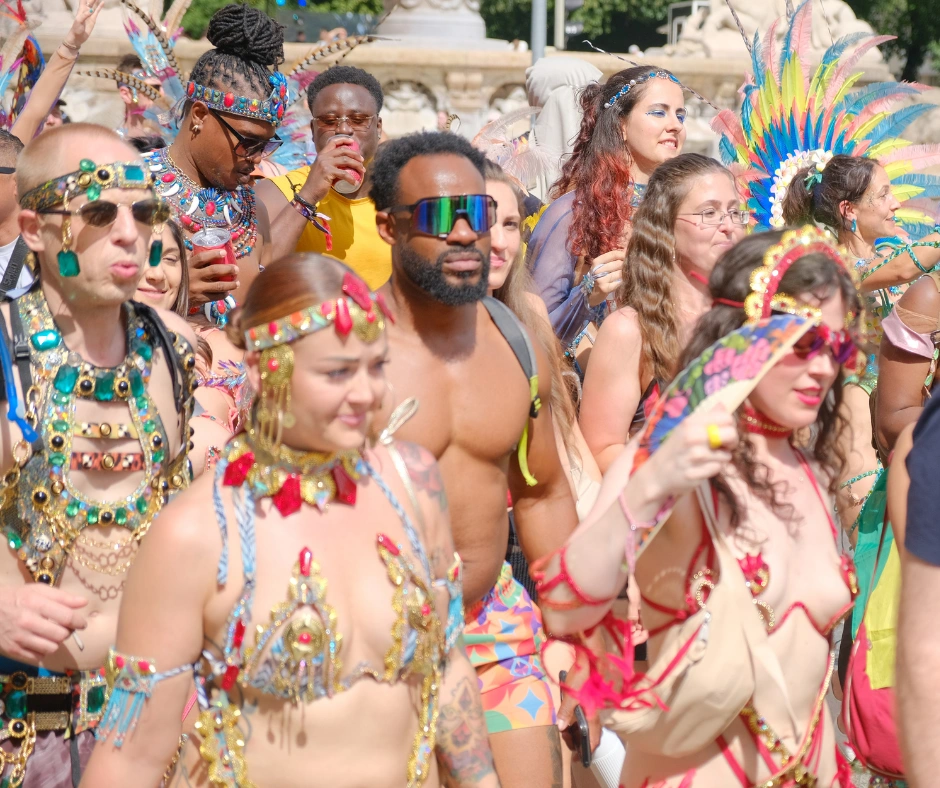 Crowd of masqueraders in gem-covered and feathered costumes gathered around an ornate stone fountain
