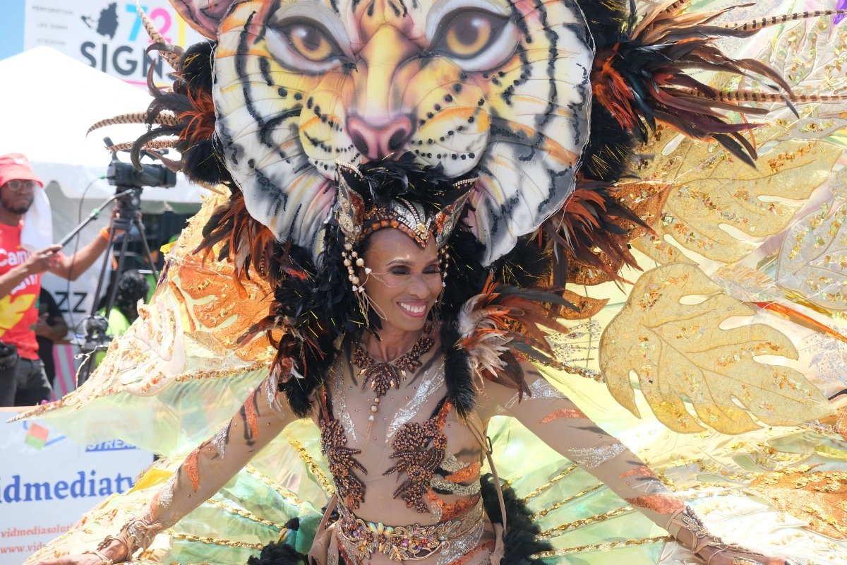Masquerader smiling in an elaborate costume with a large tiger headpiece, gold wings, and a jewelled bodice at the St. Maarten Carnival parade of bands.
