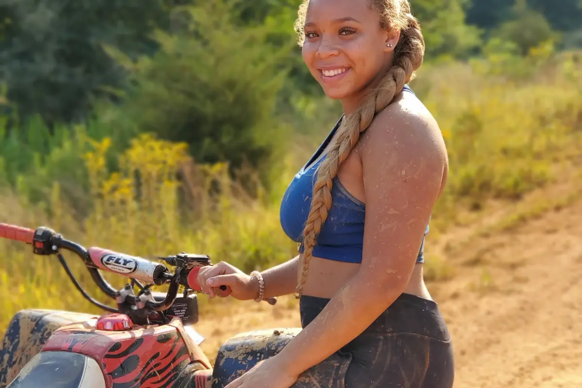 Woman covered in mud smiling beside an ATV during an off-road adventure tour in Antigua.